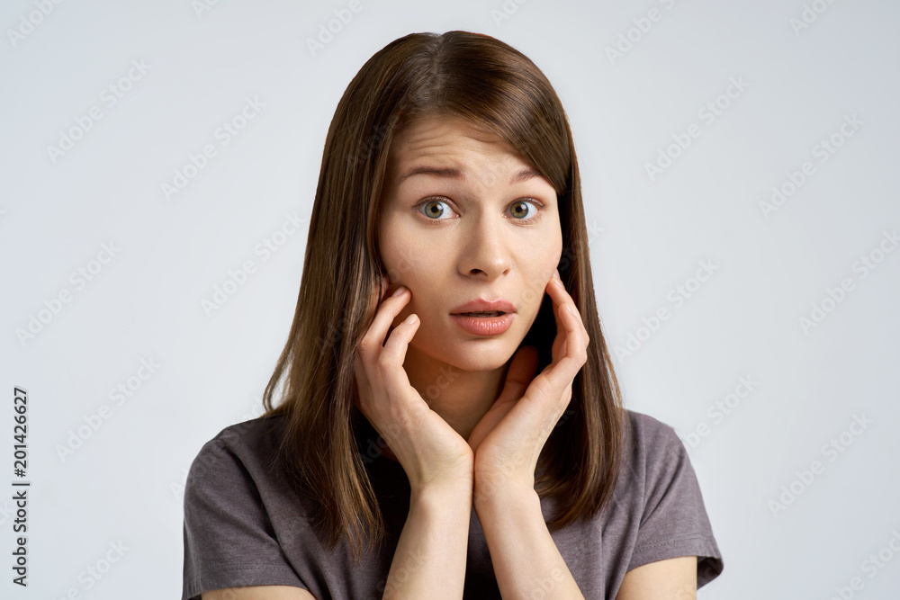 alarmed and worried young woman, the brunette looks scared in the camera and brings her palms to the cheeks. alarmed and worried young woman, the brunette looks scared in the camera and brings her palms to the cheeks.
