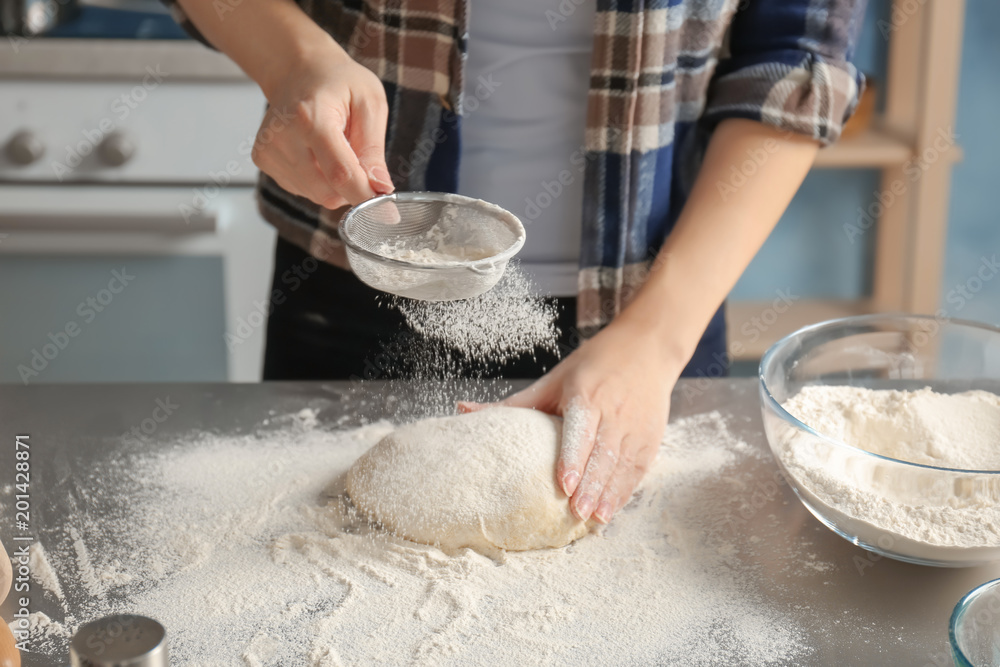 Woman sprinkling flour over dough on table in kitchen Woman sprinkling flour over dough on table in kitchen