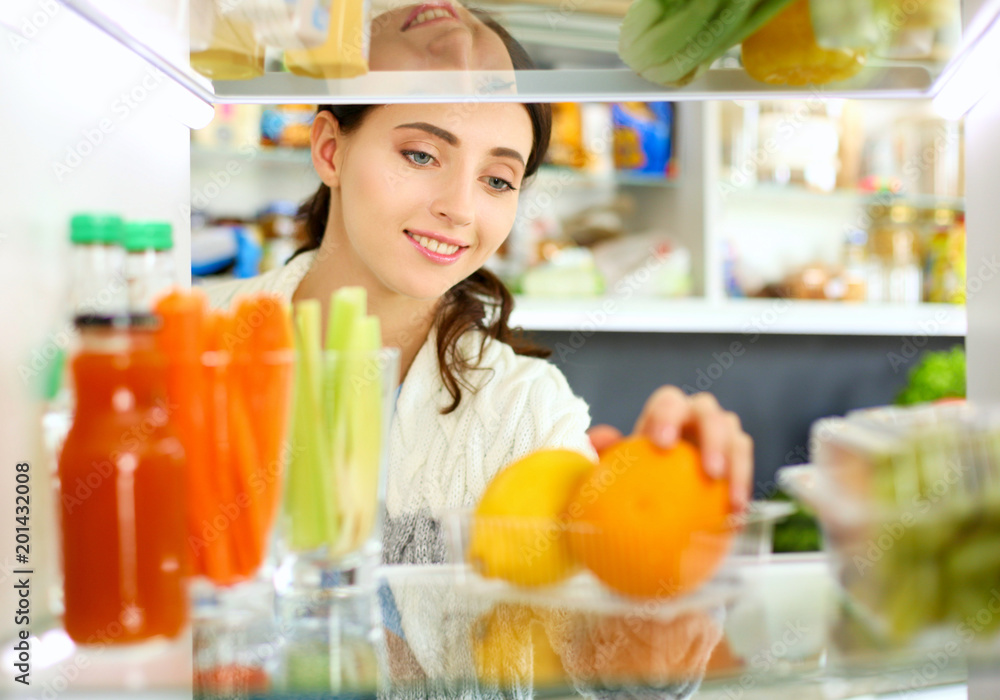 Portrait of female standing near open fridge full of healthy food, vegetables and fruits. Portrait of female Portrait of female standing near open fridge full of healthy food, vegetables and fruits. Portrait of female