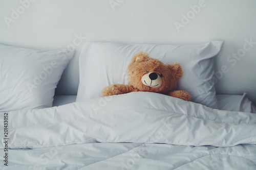 A bear doll laying on white bed.