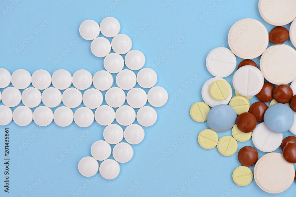 arrow of white pills and stack of tablets  on a blue background