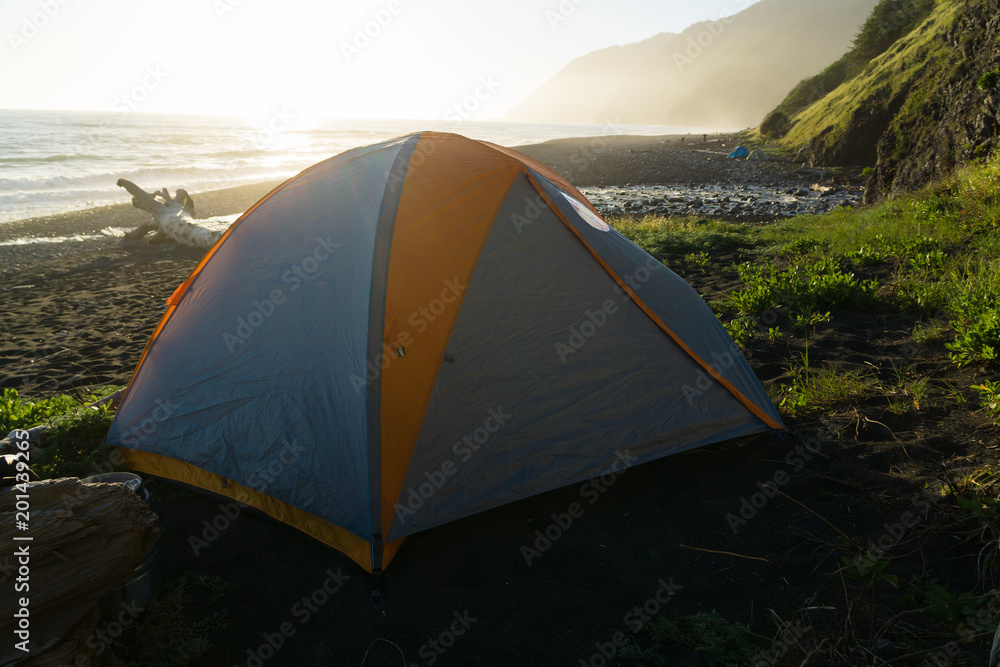 Backpacking tent sits on the black sand of the Lost Coast backpacking trail in California at sunset
