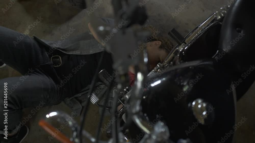 Mature woman lying on garage floor, working on motorbike, tilting up. Mature woman lying on garage floor, working on motorbike, tilting up.