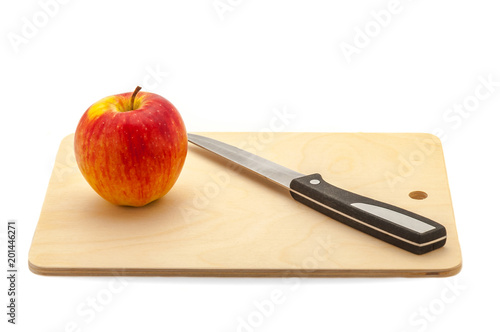 Red juicy apple and knife on a cutting board made of light wood.