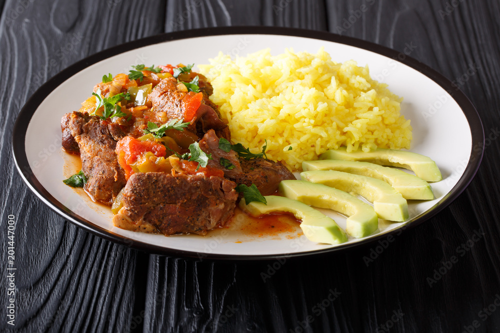 Ecuadorian traditional food: seco de chivo goat meat with a garnish of yellow rice and avocado close-up. horizontal