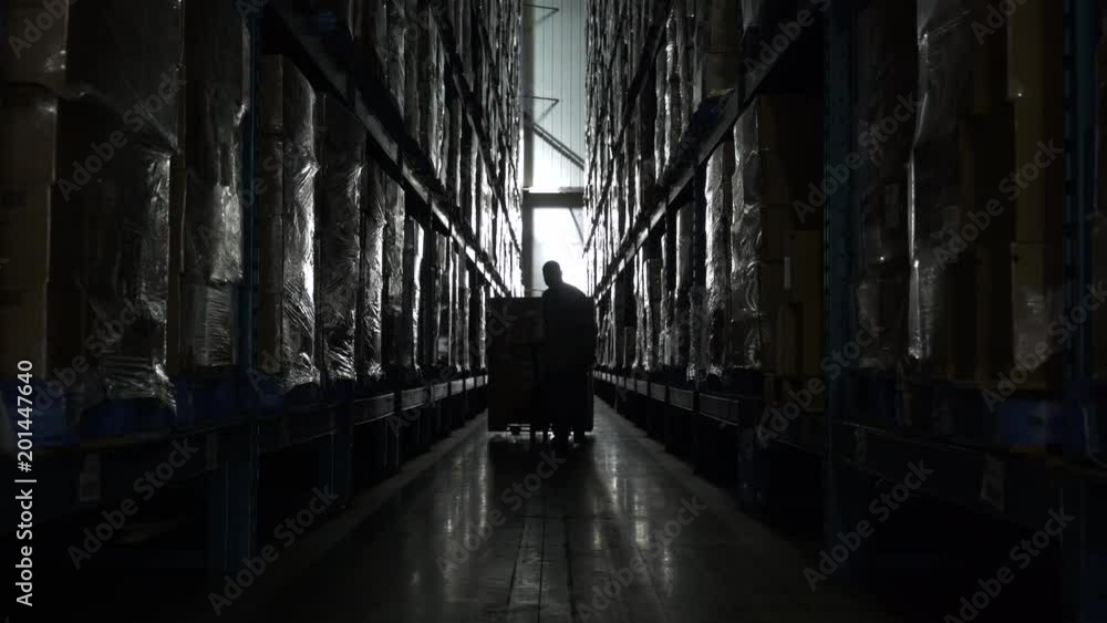 Man pulling hand held pallet truck in aisle of warehouse. Man pulling hand held pallet truck in aisle of warehouse.