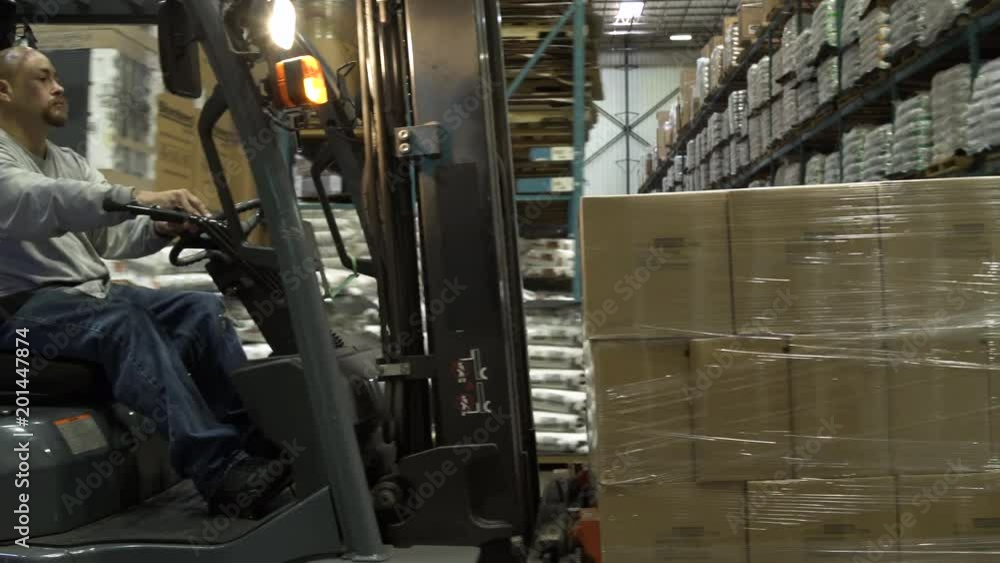 Man driving forklift machinery in warehouse, carrying and moving boxes of stock. Man driving forklift machinery in warehouse, carrying and moving boxes of stock.