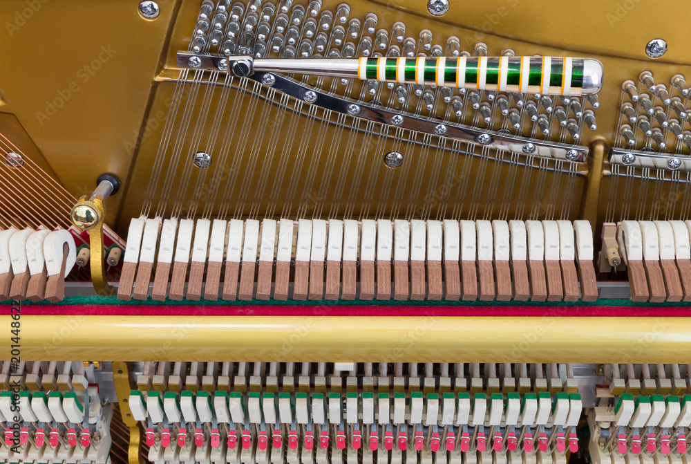 Closeup of the internal parts of an upright piano - mechanics, strings and a tuning key on the pins, front view Closeup of the internal parts of an upright piano - mechanics, strings and a tuning key on the pins, front view