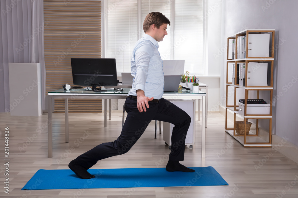 Fototapeta premium Young Businessman Doing Stretching Exercise In Office