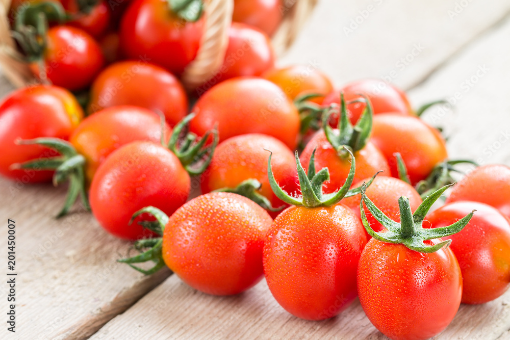 Small red cherry tomatoes spill out of a wicker basket. Small red cherry tomatoes spill out of a wicker basket.