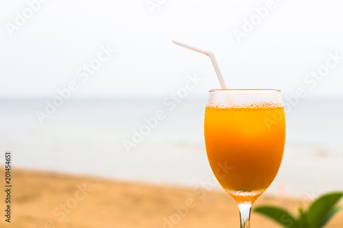 Glass of orange juice with backdrop green leaves and sand beach and sea background.