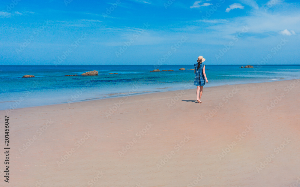 Young woman in dress walks down the white sand beach at Koh Lanta island in Thailand.