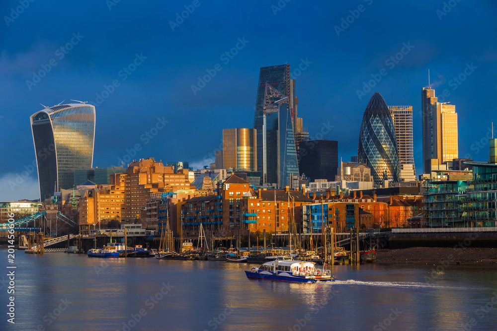 Fototapeta premium Londyn, Anglia - Skyscrapers of Bank, wiodąca dzielnica finansowa Londynu o złotej godzinie z łodzią widokową i kolorowym ciemnym niebem i chmurami