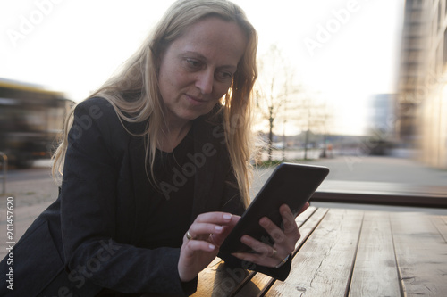 Mujer de negocios sentada en una terraza de la calle lee y escribe en su tablet.