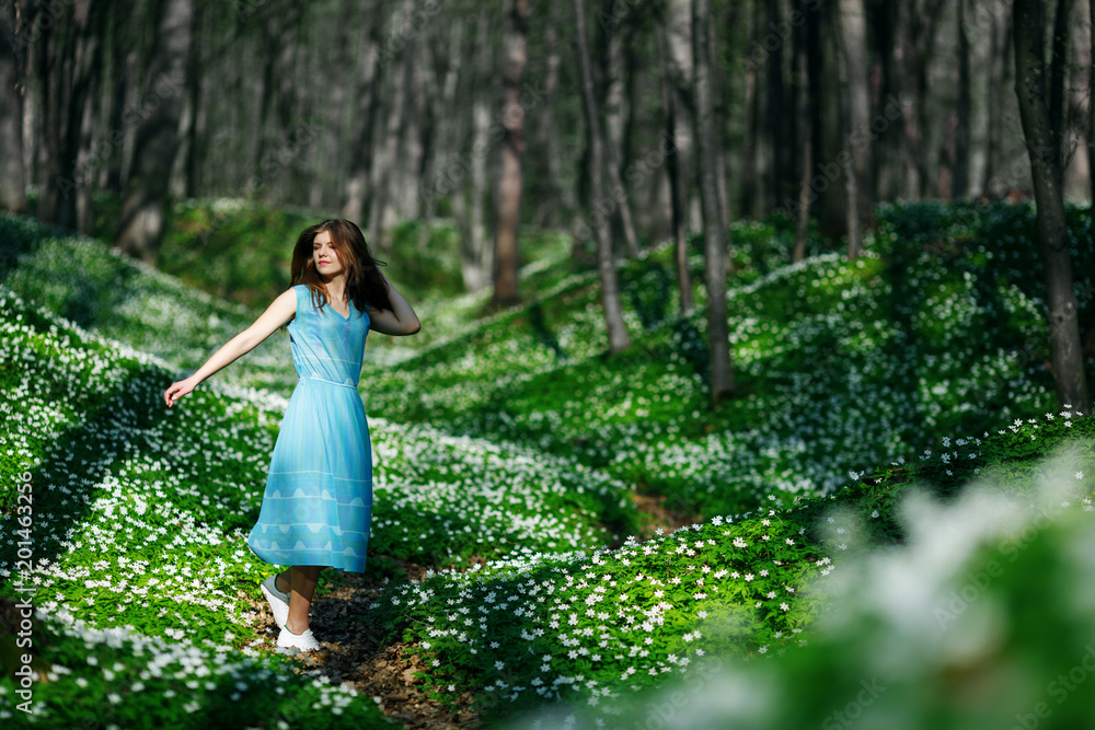 Woman runs through the forest in a long dress. Relaxing woman at nature. Happy pretty young woman enjoying smell flowers over spring forest background Woman runs through the forest in a long dress. Relaxing woman at nature. Happy pretty young woman enjoying smell flowers over spring forest background