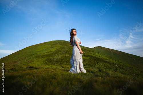 Beautiful woman in dress running in the mountains. Beautiful girl looking happy and smiling. Relaxing, feeling alive, breathing fresh air, got freedom from work. Flowers in the mountains
