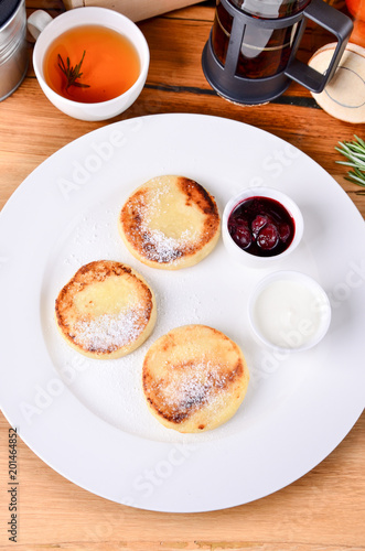Traditional russian breakfast fried cottage cheese with cherry jam, sour cream and black tea. Top view cheese pancake, close.