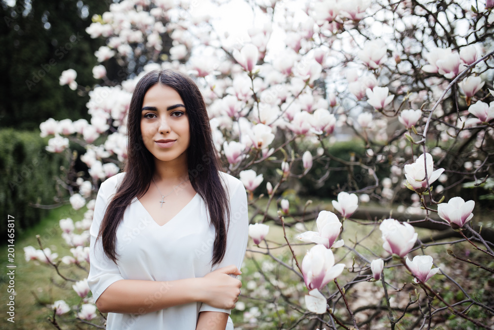 Attractive woman walks through the spring garden, enjoys the scent of flowering magnolia trees Attractive woman walks through the spring garden, enjoys the scent of flowering magnolia trees