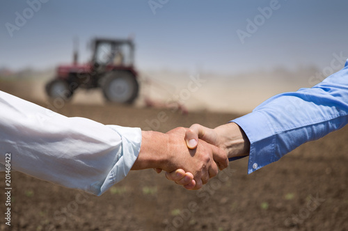 Farmers shking hands in front of tractor