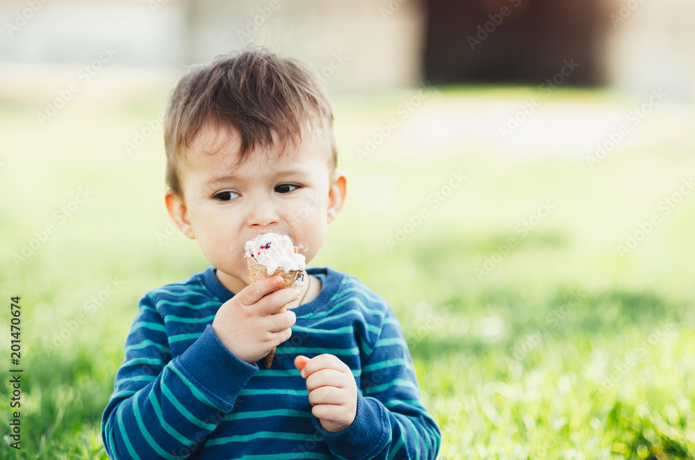 Cheerful child in a blue sweater eating ice cream on a background of grass, outdoors Cheerful child in a blue sweater eating ice cream on a background of grass, outdoors