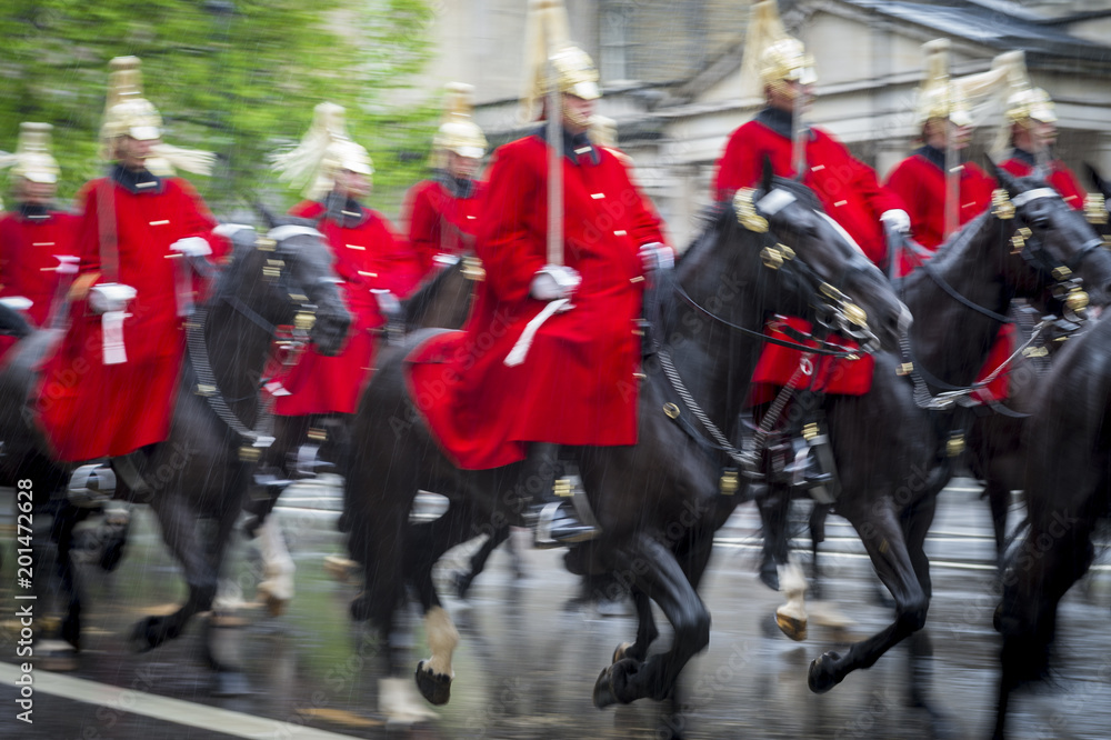 Royal guards on horseback dressed in ceremonial red coats pass with motion blur in a parade on a