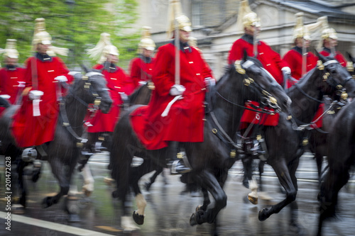 Royal guards on horseback dressed in ceremonial red coats pass with motion blur in a parade on a rainy day in London, England, UK. Shot with slow shutter speed.