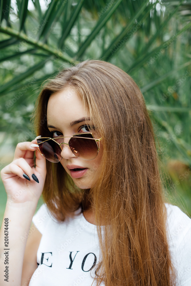 Fashion Portrait of Stylish Beautiful Girl in Palm Trees. Beautiful Young Cute Brunette Model Gil in Summer Bright Casual Hipster Clothes. Fashion Portrait of Stylish Beautiful Girl in Palm Trees. Beautiful Young Cute Brunette Model Gil in Summer Bright Casual Hipster Clothes.
