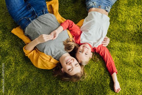 top view of happy mother and daughter lying together and smiling at camera