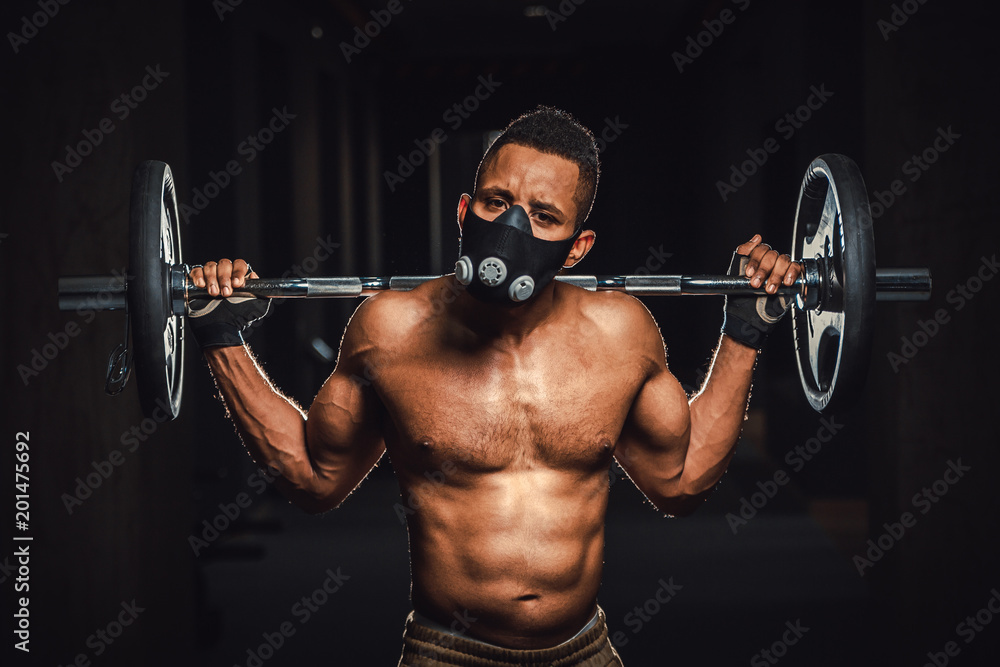 african american athletic strong man holding barbell on shoulders in gym. black man poses with barbell in gym close-up african american athletic strong man holding barbell on shoulders in gym. black man poses with barbell in gym close-up