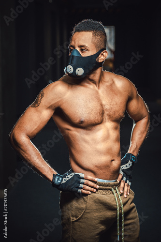 african american athletic man in mask looking away and holds hands on belt. black man in gym. black background