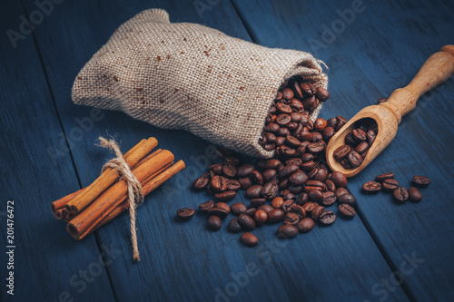 Fried coffee beans in a sackbag and wooden spoon on a blue textured background with copy space. Minimalist design for advertising in a cafe, top view. photo