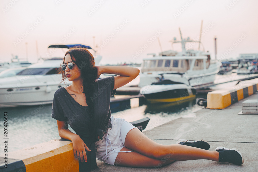 Fashion Portrait of Beautiful Sexy Girl. Posing on Yacht Club at Europe. Young Pretty Hipster Woman with Long Dark Brown Hair Color, Big Lips and Sunglasses. Film Color, Grain and Effects 