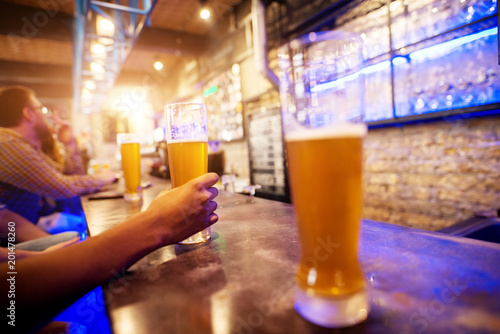 Wallpaper Mural Close up view of hand while holding draft beer glass placed on a bar table with a row of other in the background. Torontodigital.ca