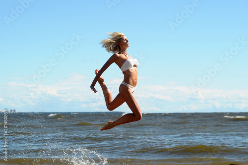 beautiful blonde in a swimsuit is jumping near the sea photo