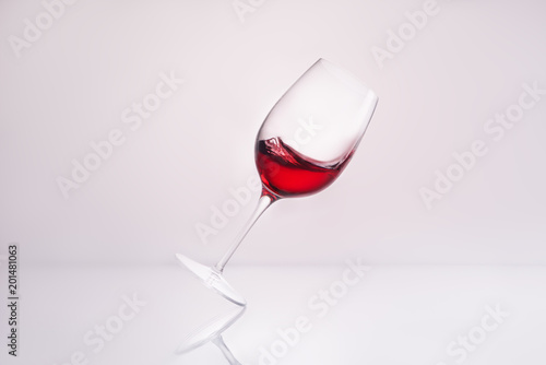 Canvastavla inclined wineglass with delicious red wine on reflective surface and on white