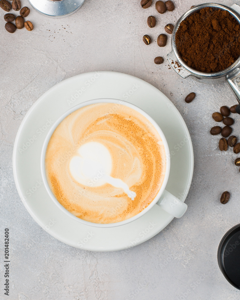 The cup of latte or cappuccino coffee with milk. Background with tools for making fresh boiled coffee: a glass of milk, coffee beans, a horn from a coffee machine. - obrazy, fototapety, plakaty 