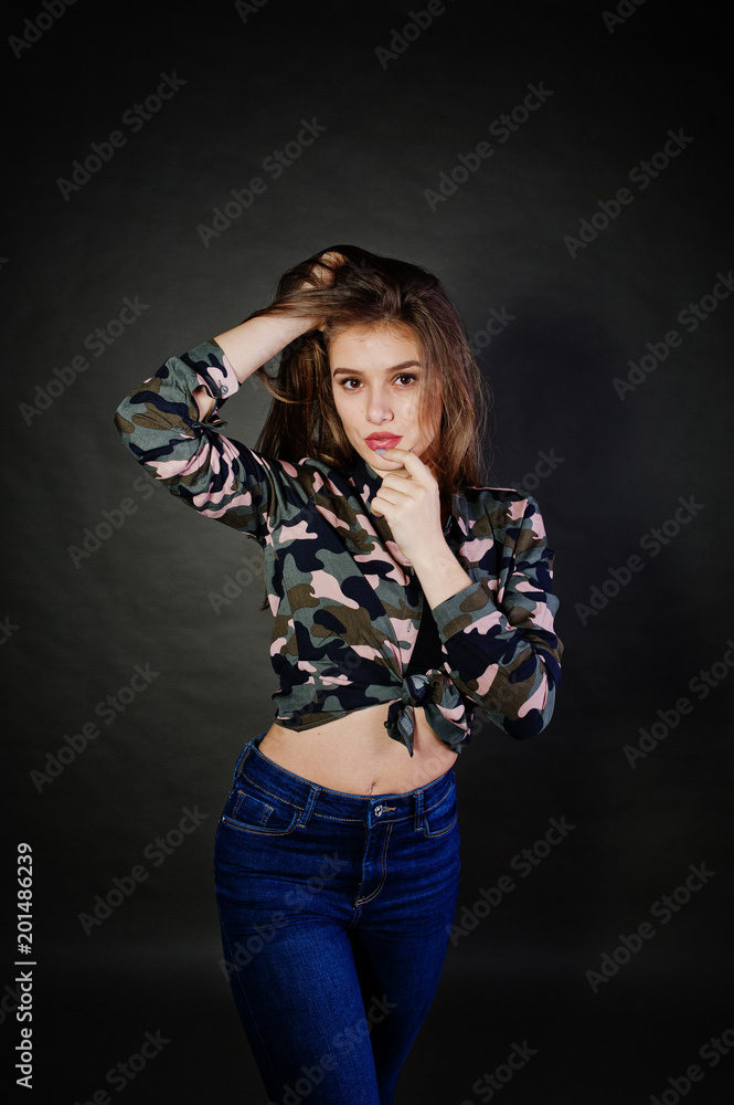 Handsome brunette girl wear military shirt and jeans, posing at studio against gray background. Studio model portrait. Handsome brunette girl wear military shirt and jeans, posing at studio against gray background. Studio model portrait.