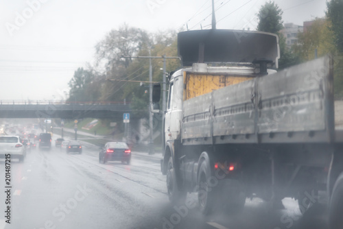 Big truck with empty trailer for commercial industrial cargo on a multi-lines highway with wet shiny coating and rain dust in rainy weather photo