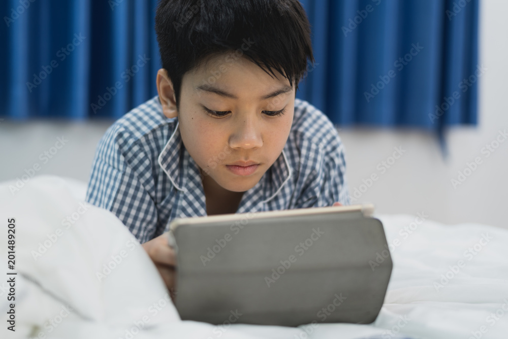 Cut boy lying on the bed with a table. Child playing with digital tablet lying on a bed. Cut boy lying on the bed with a table. Child playing with digital tablet lying on a bed.