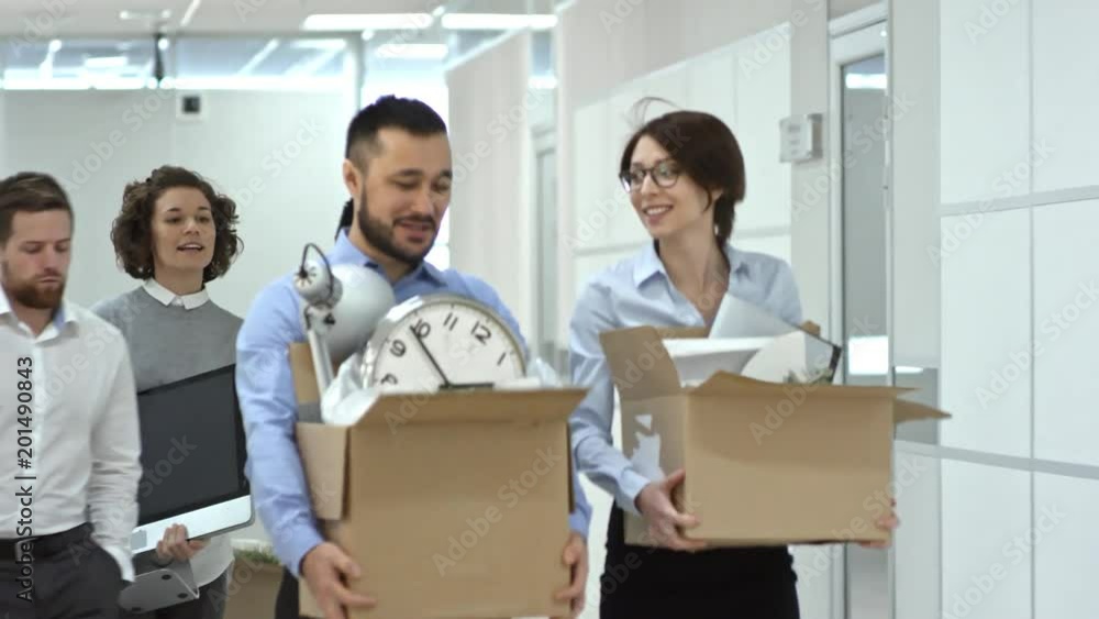 Multi-ethnic team of office workers walking through hallway towards the camera while moving into new office, chatting and carrying belongings Multi-ethnic team of office workers walking through hallway towards the camera while moving into new office, chatting and carrying belongings