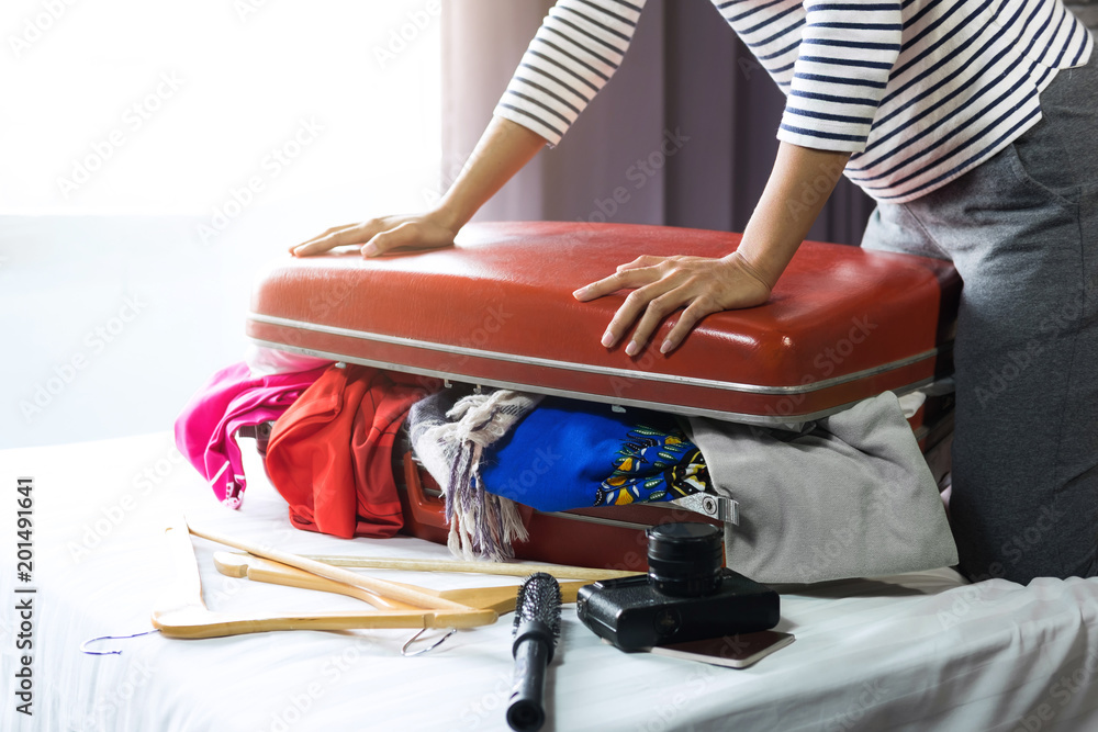 Travel and vacation concept, happiness young woman packing a lot of her clothes and stuff into suitcase on bed prepare for travel and journey trip in holiday