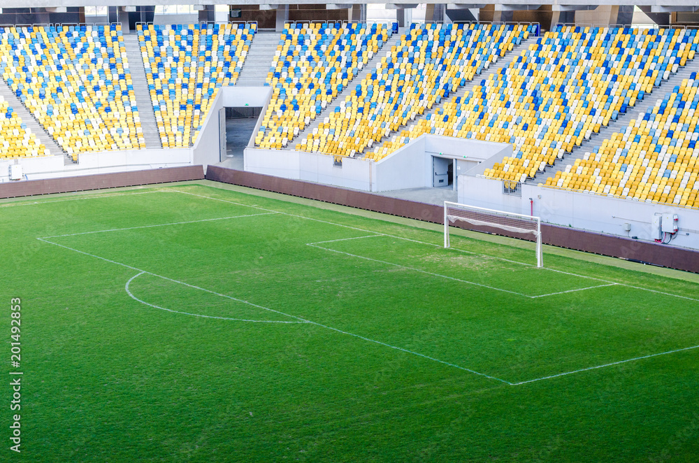 Fototapeta premium Siedzący kibice kolorowe plastikowe krzesła na tle stadionu piłkarskiego. Pusty stadion boisko do piłki nożnej zielona trawa na arenie lekkoatletycznej piłki nożnej.