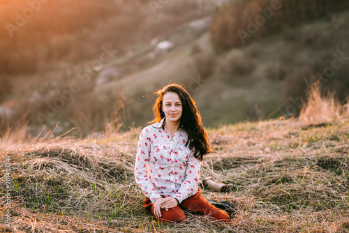 Beautiful girl in the mountains at sunset. The girl is sitting on the grass on the top