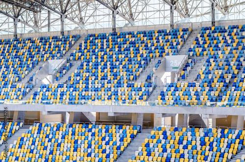 Sitting fans colored plastic chairs at the football stadium background. Empty stadium football field green grass for soccer athletics arena.