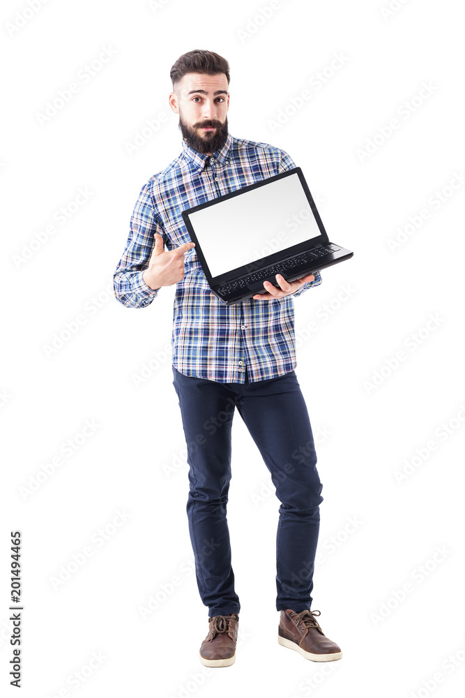 Stylish bearded young man pointing finger on blank laptop screen looking at camera. Full body isolated on white background. Stylish bearded young man pointing finger on blank laptop screen looking at camera. Full body isolated on white background.