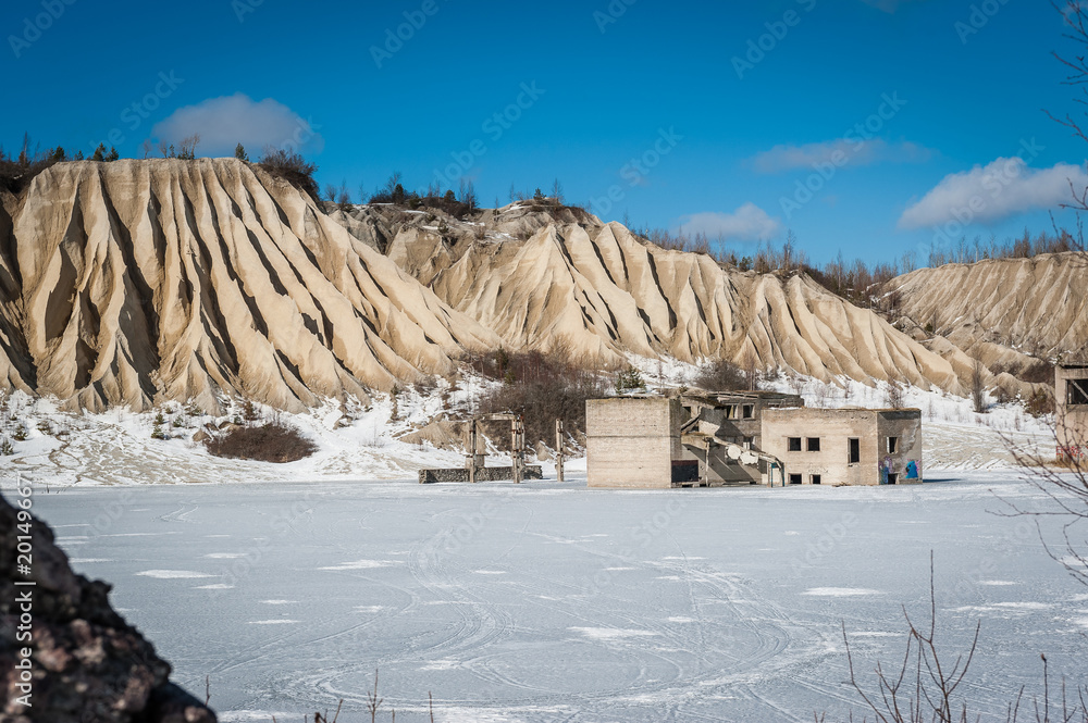 View of abandoned prison located in small lake with blue clear water in Rummu, Estonia. Ruins on ex industry place in old stone building. Winter. Slag heap.