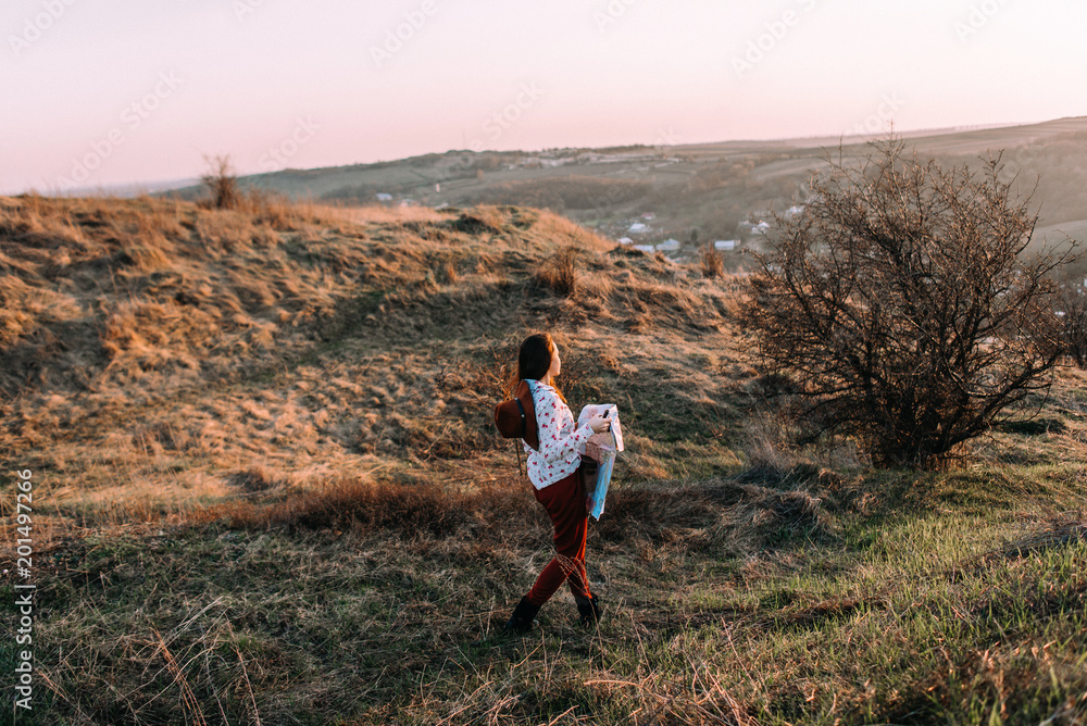 Traveler beautiful girl with a hat, binoculars and map looking into the distance in sunset on a background of mountains. Wearing stylish fall outfit. Concept photo travel, adventure