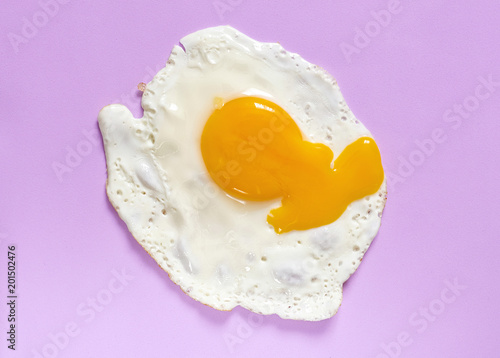Fried egg with broken yolk on a lavender background. Flat lay, copy space