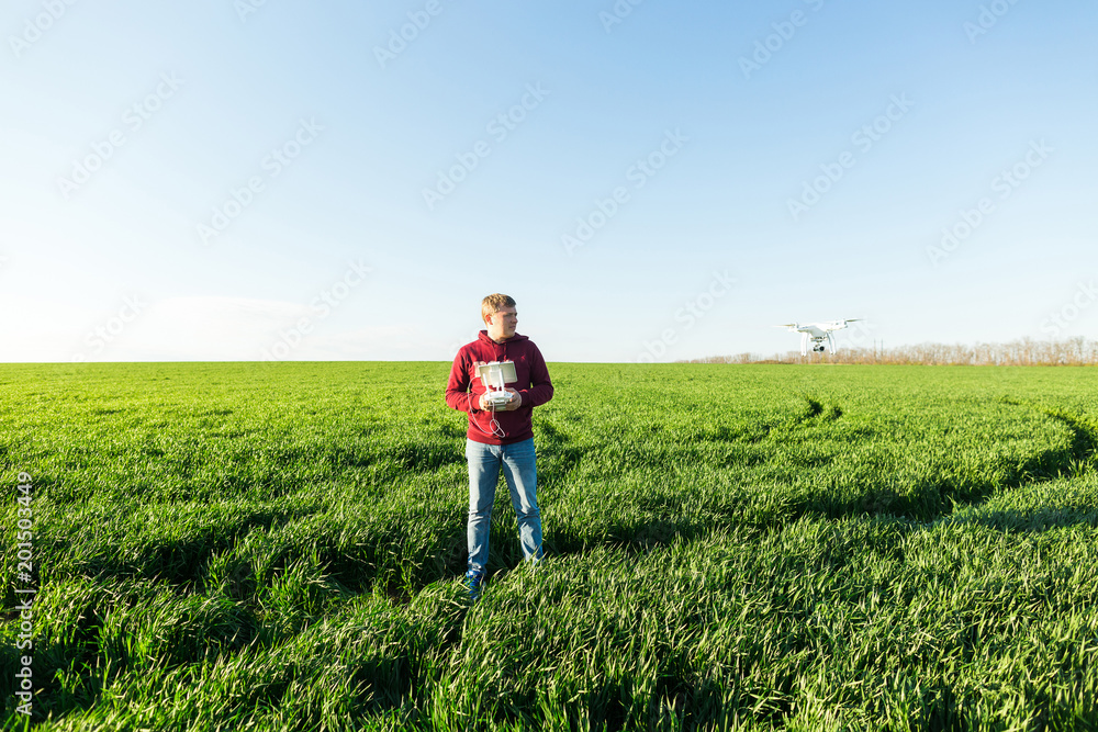 quadcopter outdoors, aerial imagery and recreation concept - male man in jeans and fleece hoodie controls the flight altitude of superb white drone, background of blue sky and field of green grass. quadcopter outdoors, aerial imagery and recreation concept - male man in jeans and fleece hoodie controls the flight altitude of superb white drone, background of blue sky and field of green grass.