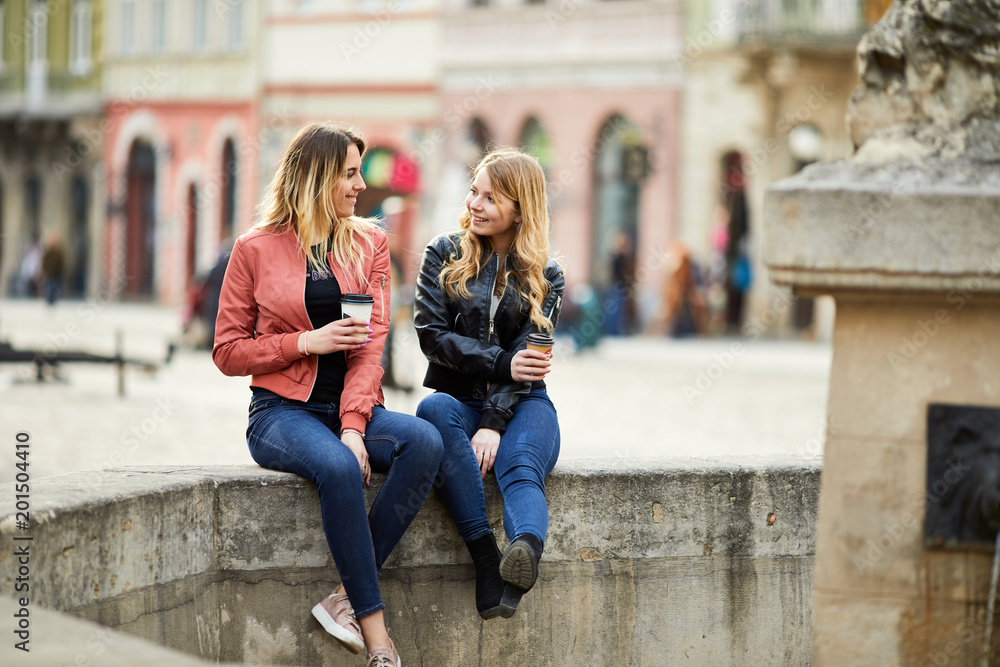 Two girls sit on the fountain and talk to each other